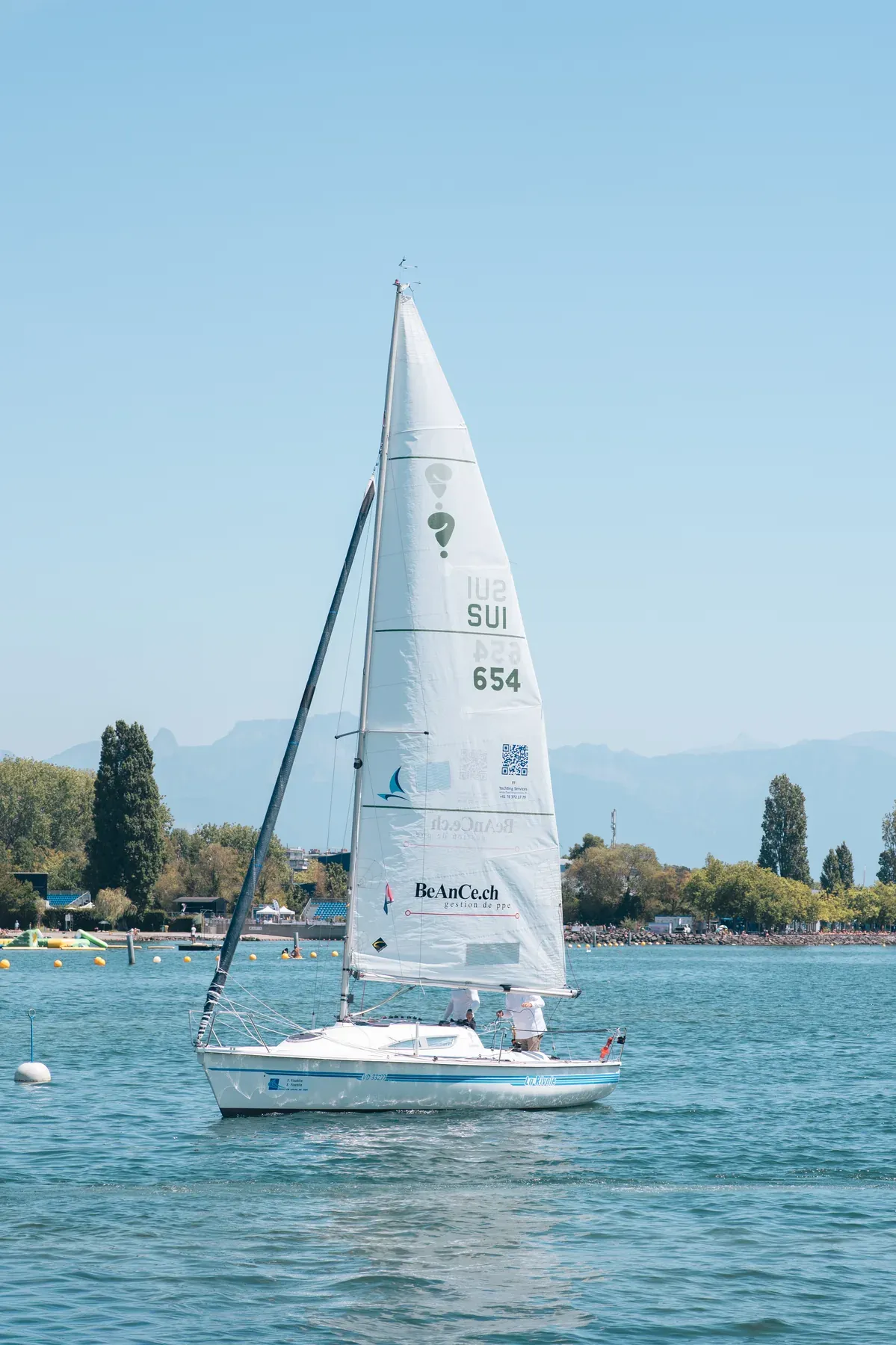 La Rivale 3 naviguant sur le Léman, sa grand-voile entière visible devant les montagnes
